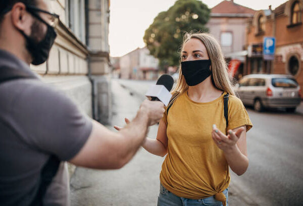 Man and woman, two people with black face masks on the street, man news reporter interviewing a woman on the street